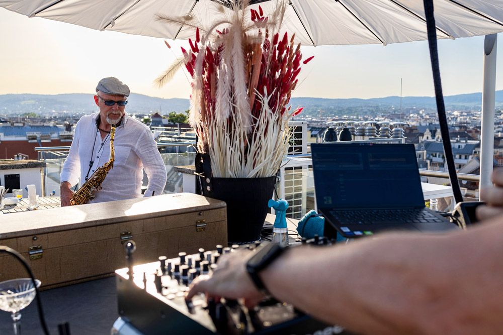 Mischpult im Vordergrund und Saxophonist im Hintergrund auf einer Rooftop Terrasse