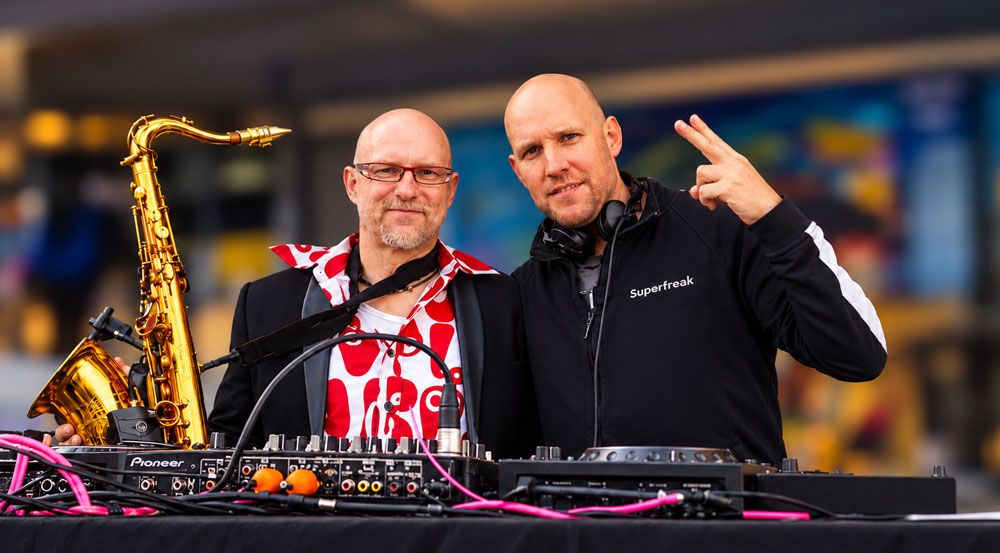 DJ und Saxophonist hinter dem Mischpult vor einer Discokugel